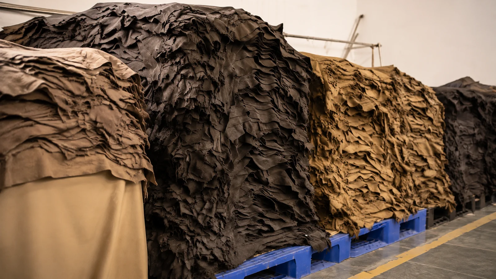 Stacks of brown, tan, and black leather skins arranged on blue pallets.