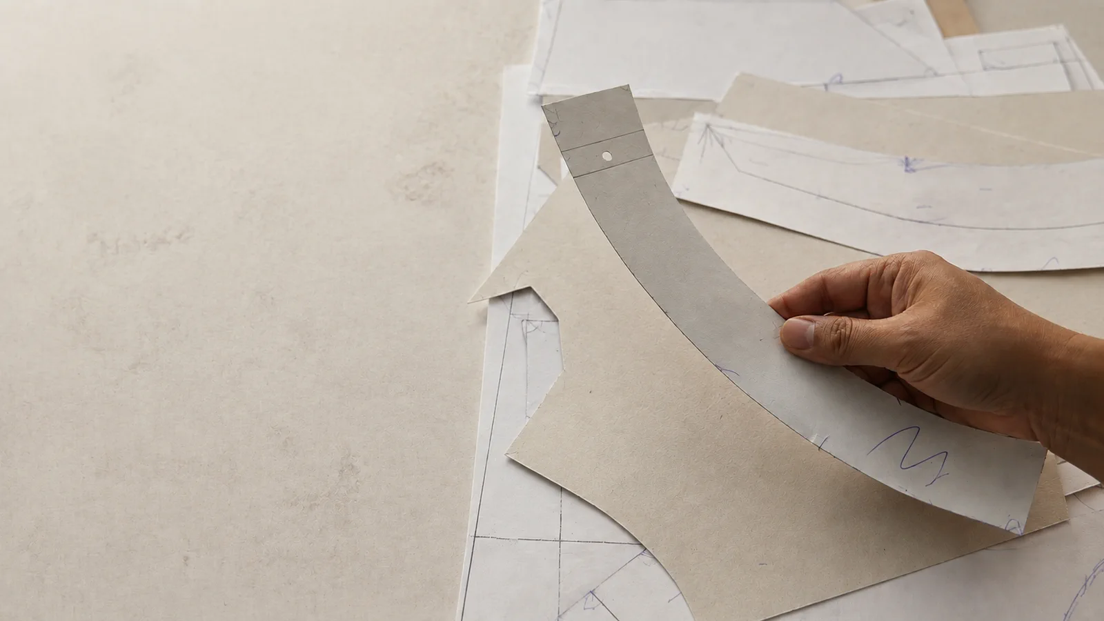 Hands reviewing layered garment pattern pieces on a development table.