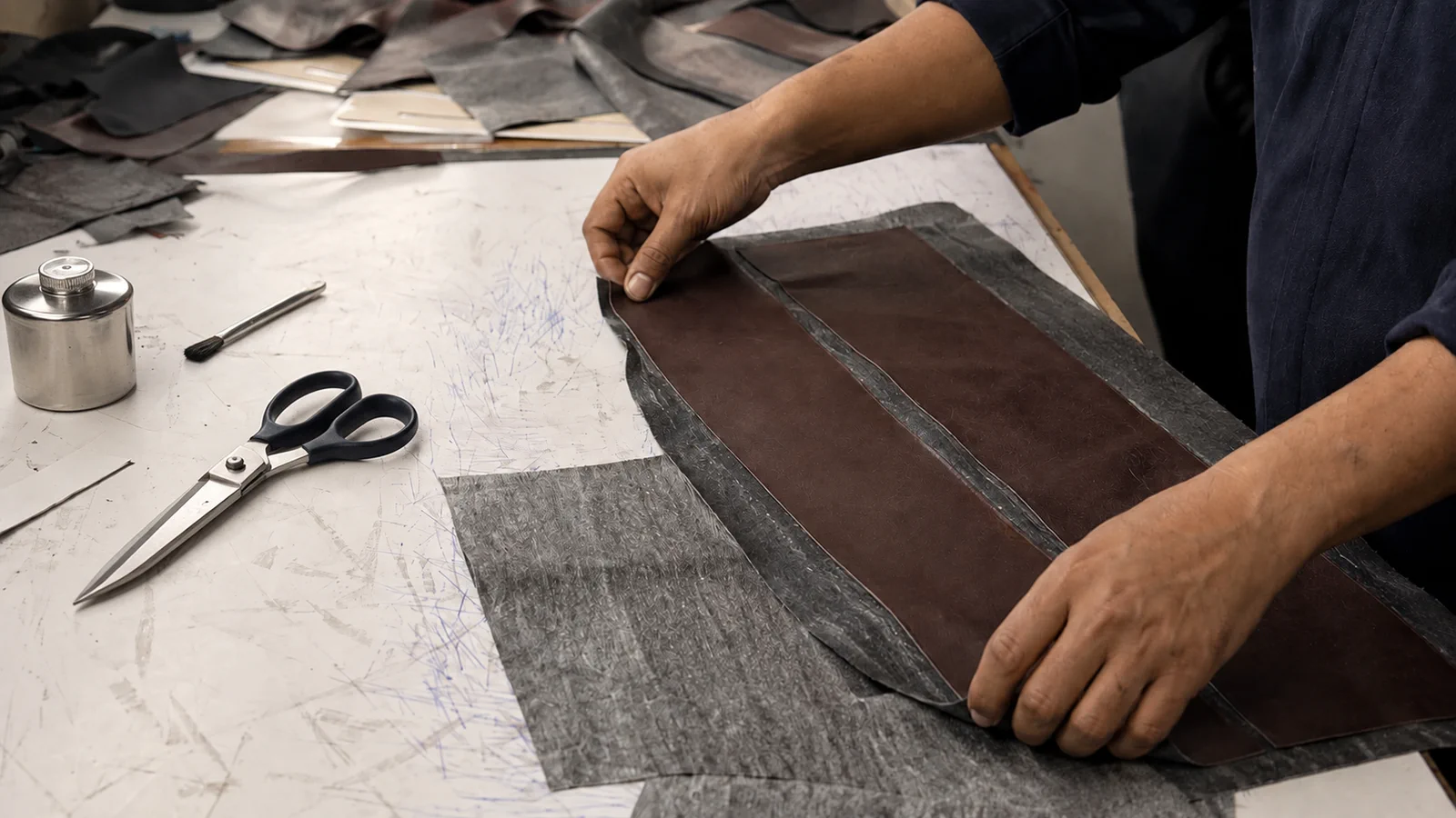Hands aligning leather components beside cutting and marking tools.