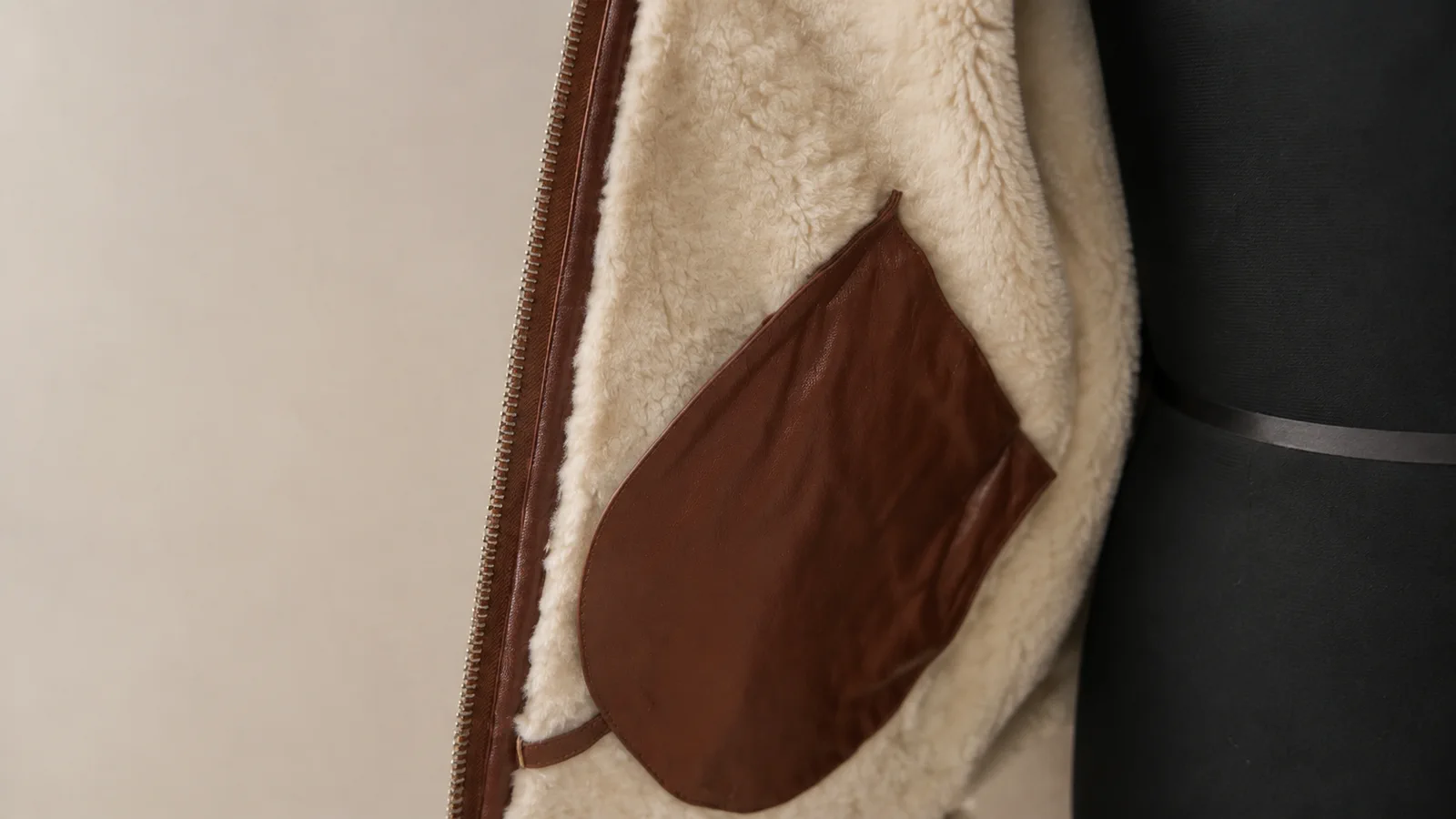 Close view of a shearling jacket lining, internal pocket, zipper, and leather edge.